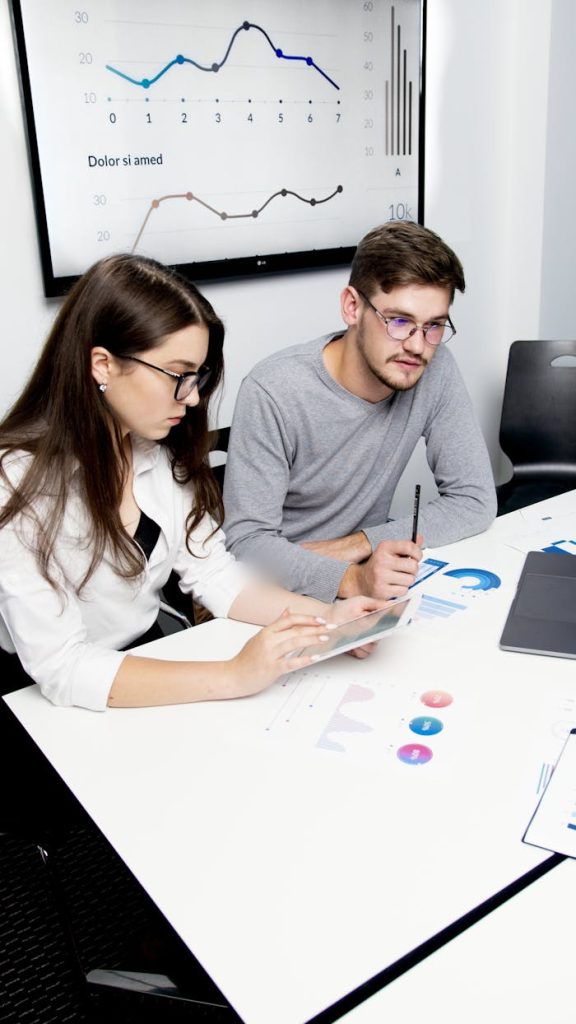 woman-in-gray-long-sleeve-shirt-holding-pen-writing-on-white-paper-5715844 Two business professionals collaborating on financial analysis with charts and graphs.